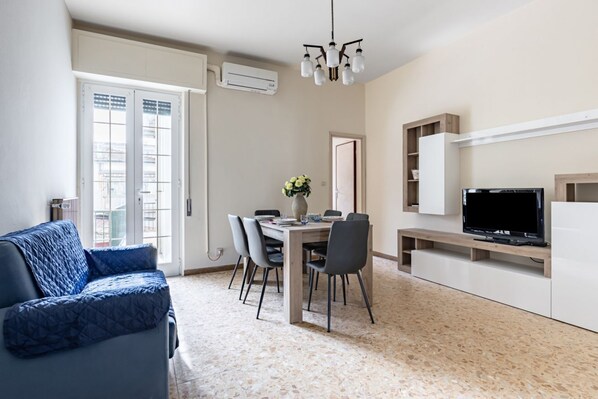 A modern living room with a sofa, a dining table with chairs, a TV, and a built-in shelf.