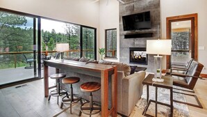 A modern living room with a large window, a fireplace, a TV, and a seating area. - Custom home close to ski resort with hot tub (Angel Fire)
