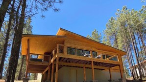 A two-story wooden cabin with a balcony, surrounded by trees. - Custom home close to ski resort with hot tub (Angel Fire)