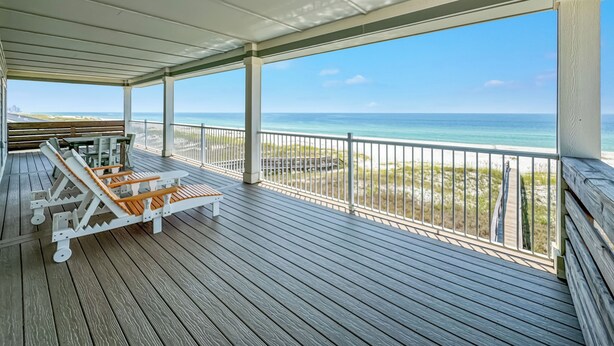 A covered deck with wooden flooring, white railings, and a view of the ocean. - "Sandy Feet Retreat" | Beachfront | Private Pool | Beach Getaways (Pensacola)