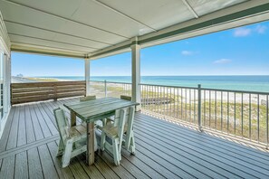 A covered outdoor area with a wooden table and chairs, a bench, and a view of the ocean. - "Sandy Feet Retreat" | Beachfront | Private Pool | Beach Getaways (Pensacola)