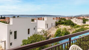 A residential area with modern white buildings, a clear view of the sea, and a balcony with a chair. - 1 bedroom awesome apartment in Kastel Kambelovac (Kastel Kambelovac)