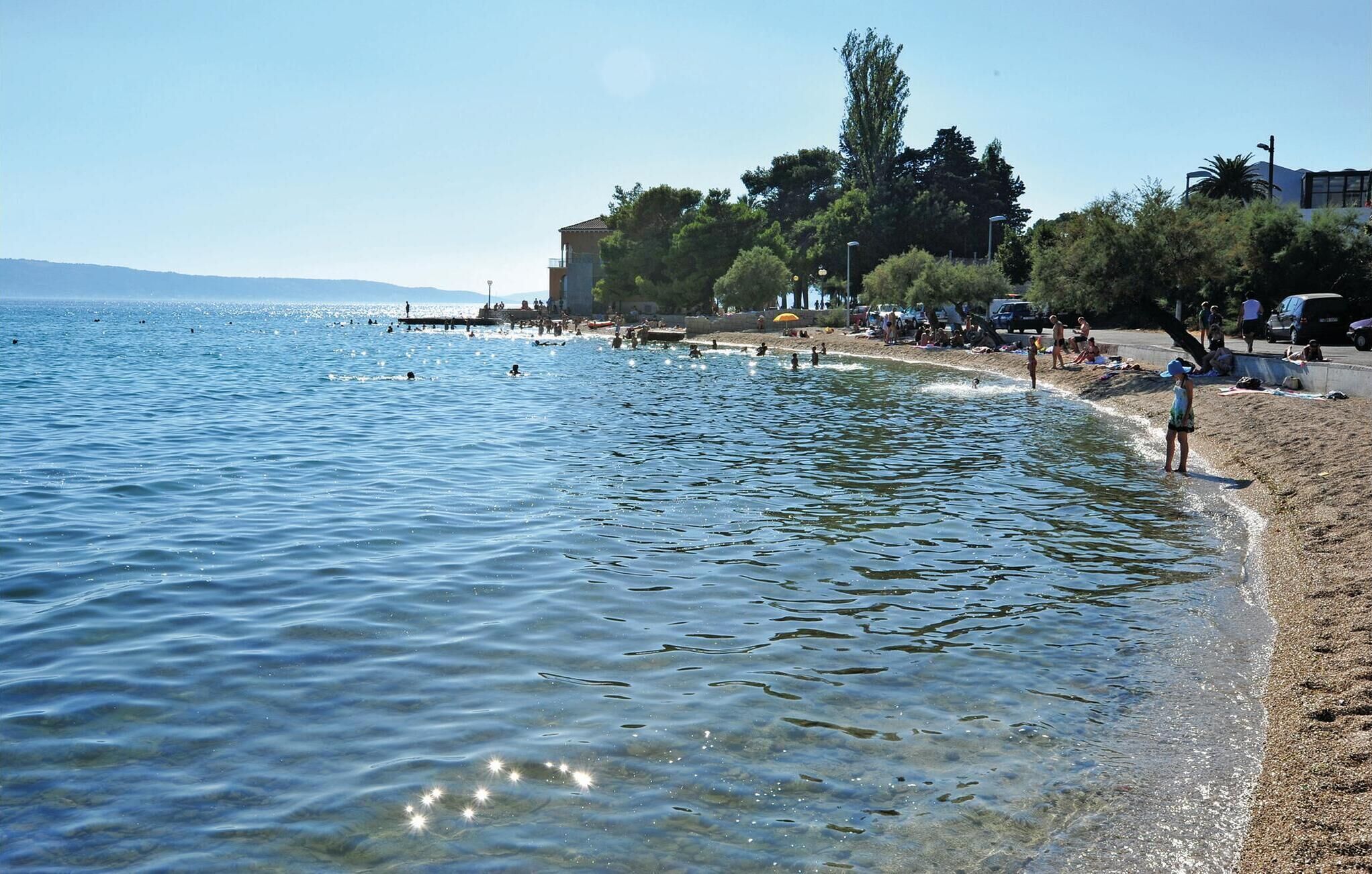 A beach with clear water, a pier, and people enjoying the area.