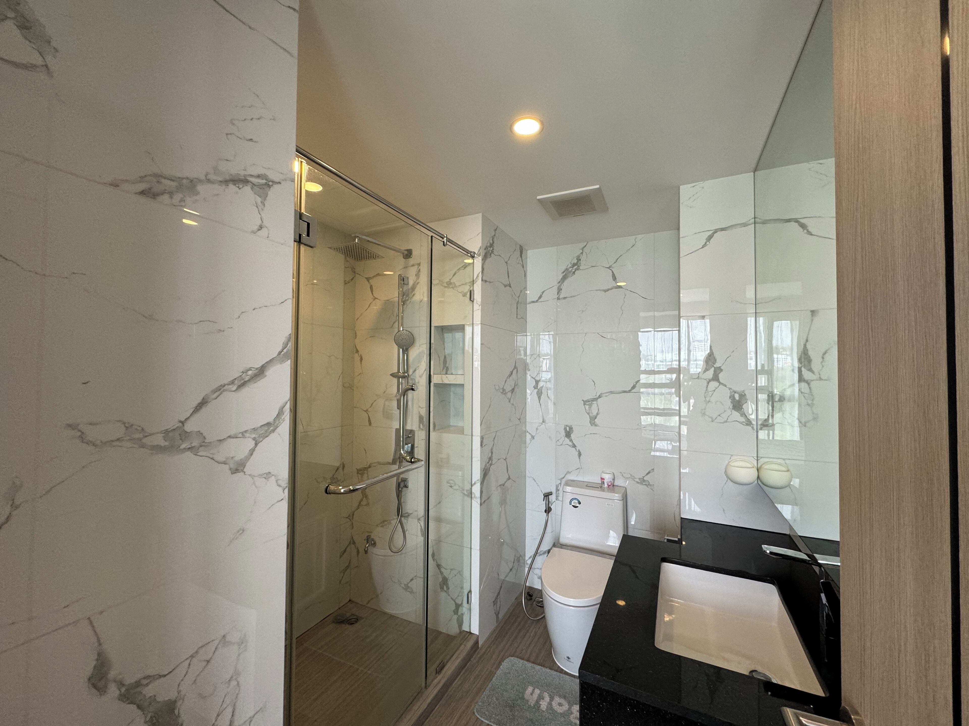 A modern bathroom with a glass-enclosed shower, a toilet, and a black sink.