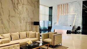 A modern lobby with a marble wall, a sofa, armchairs, a coffee table, and a reception desk. - The Panora Pattaya by PSR (Pattaya)