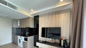A modern kitchen with a built-in washer and dryer, a large flat-screen TV, and a wooden accent wall. - The Panora Pattaya by PSR (Pattaya)