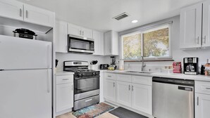 A modern kitchen with white cabinets, stainless steel appliances, and a window with blinds. - Oasis Condo on the fairway; fast WiFi, smart TVs, spectacular golf course views (Victorville)