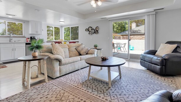 A spacious living area with a sofa, coffee table, and a black leather chair. There is a kitchen area with cabinets and a ceiling fan. - Oasis Condo on the fairway; fast WiFi, smart TVs, spectacular golf course views (Victorville)