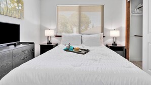 A neatly made bed with a tray of food and glasses, a TV, and a painting on the wall. - Oasis Condo on the fairway; fast WiFi, smart TVs, spectacular golf course views (Victorville)
