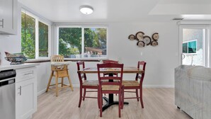 A modern kitchen with white cabinets, a dining table with four chairs, and a large window with blinds. - Oasis Condo on the fairway; fast WiFi, smart TVs, spectacular golf course views (Victorville)