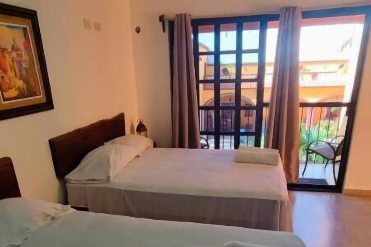 Habitación de hotel con dos camas, ventilador de techo, ventana con cortinas y vista al exterior.