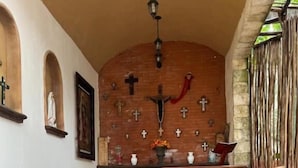 Ein Kircheninneres mit einer hölzernen Kirchenbank im Vordergrund, einem steinernen Altar mit Kruzifix und mehreren Kreuzen an der Wand.