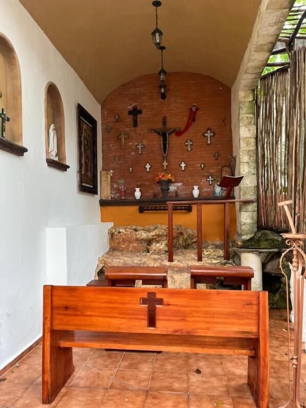 Interior de iglesia con un banco de madera al frente, un altar de piedra con un crucifijo y varias cruces en la pared.