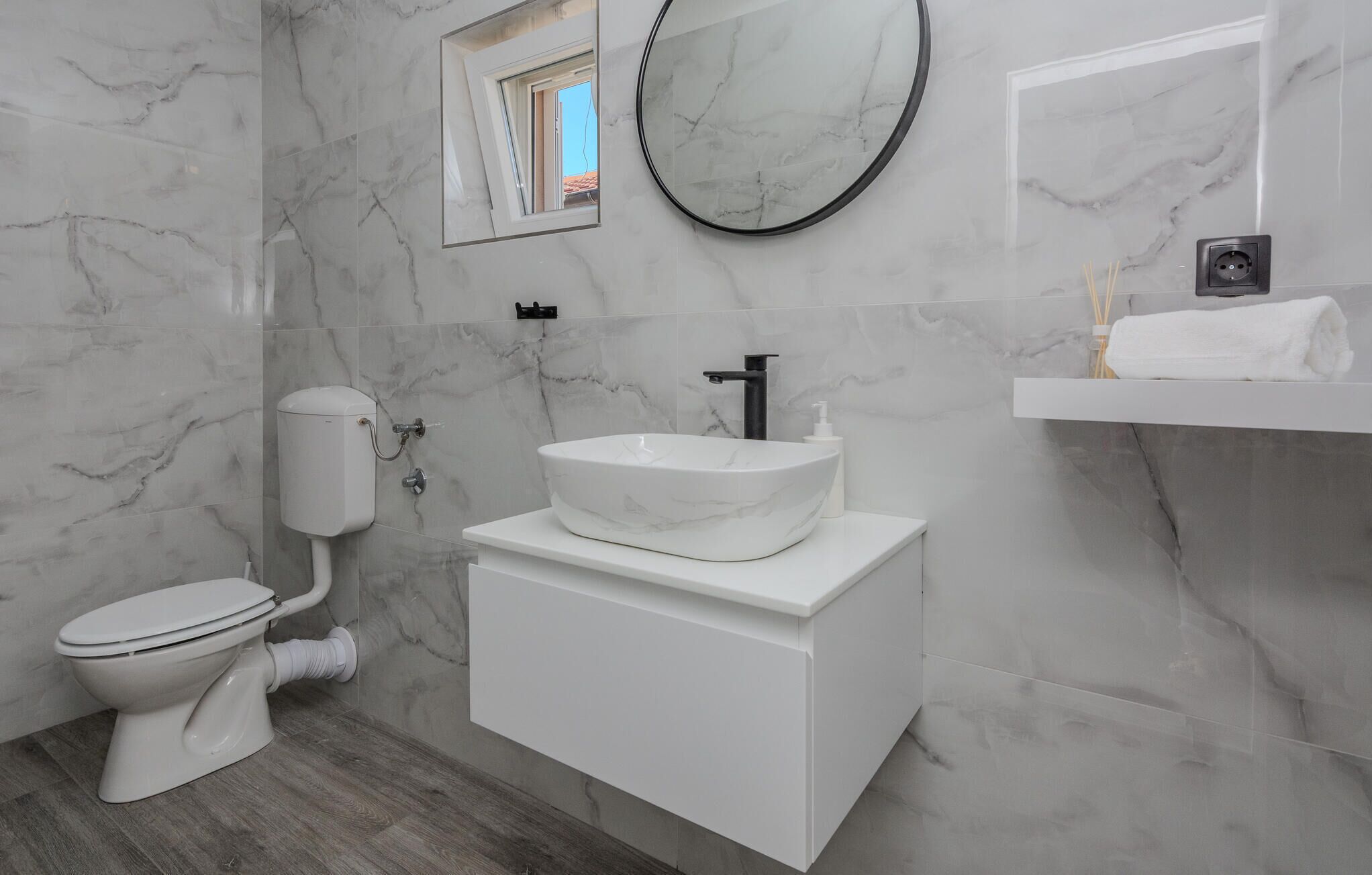 Een badkamer met toilet, wastafel, spiegel en handdoekhouder.