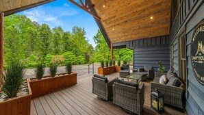 A covered outdoor area with wooden flooring, wicker furniture, and planters. - Family Escape w/Golf Sim, Pool, Theater, Arcade (Sevierville)