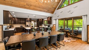 A spacious kitchen with dark wooden cabinets, a large island, and a dining area with a long wooden table and leather chairs. - Family Escape w/Golf Sim, Pool, Theater, Arcade (Sevierville)