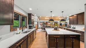 A modern kitchen with dark wood cabinets, a large island, and a view of the outdoors. - Family Escape w/Golf Sim, Pool, Theater, Arcade (Sevierville)