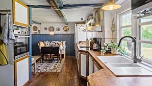 A compact kitchen with a wooden floor, a dining area with a patterned rug, and a large window providing natural light. - 4 bedroom gorgeous home in Rødby (Rødby)