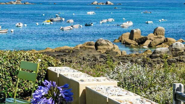 A coastal view with boats on the water, rocky shore, and a chair with flowers. - Les Pieds dans l'eau by Interhome (Cléder)