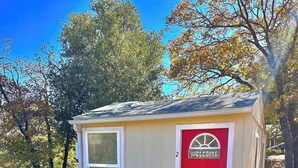 A small, single-story structure with a red door and a welcome sign. - Cozy and Quiet Tiny House Cottage with Skylight 2 Minutes from Main Street (Julian)