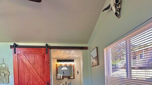 A room with a red barn-style door, a white pedestal sink, a bench, and a large window with blinds. - Cozy and Quiet Tiny House Cottage with Skylight 2 Minutes from Main Street (Julian)
