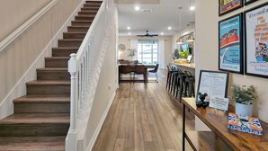 A modern interior with a wooden staircase, a dining area, and a reception desk with framed posters. - Sunset Getaway ~ Game-room, Pool, Close to Disney (Davenport)