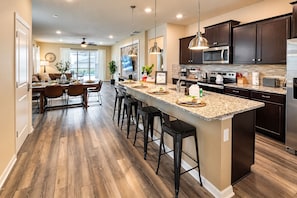A modern kitchen with a central island, dark cabinetry, stainless steel appliances, and a dining area with a view.