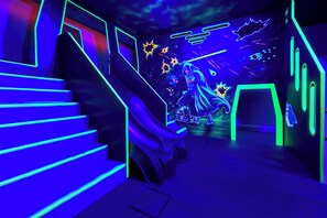 A futuristic room with a neon-lit staircase and a wall featuring a character in a hooded cloak.