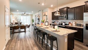 A modern kitchen with a large island, dark cabinetry, and stainless steel appliances. - Sunset Getaway ~ Game-room, Pool, Close to Disney (Davenport)
