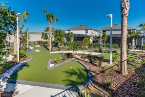 A miniature golf course with a green putting area, surrounded by palm trees and a residential neighborhood.