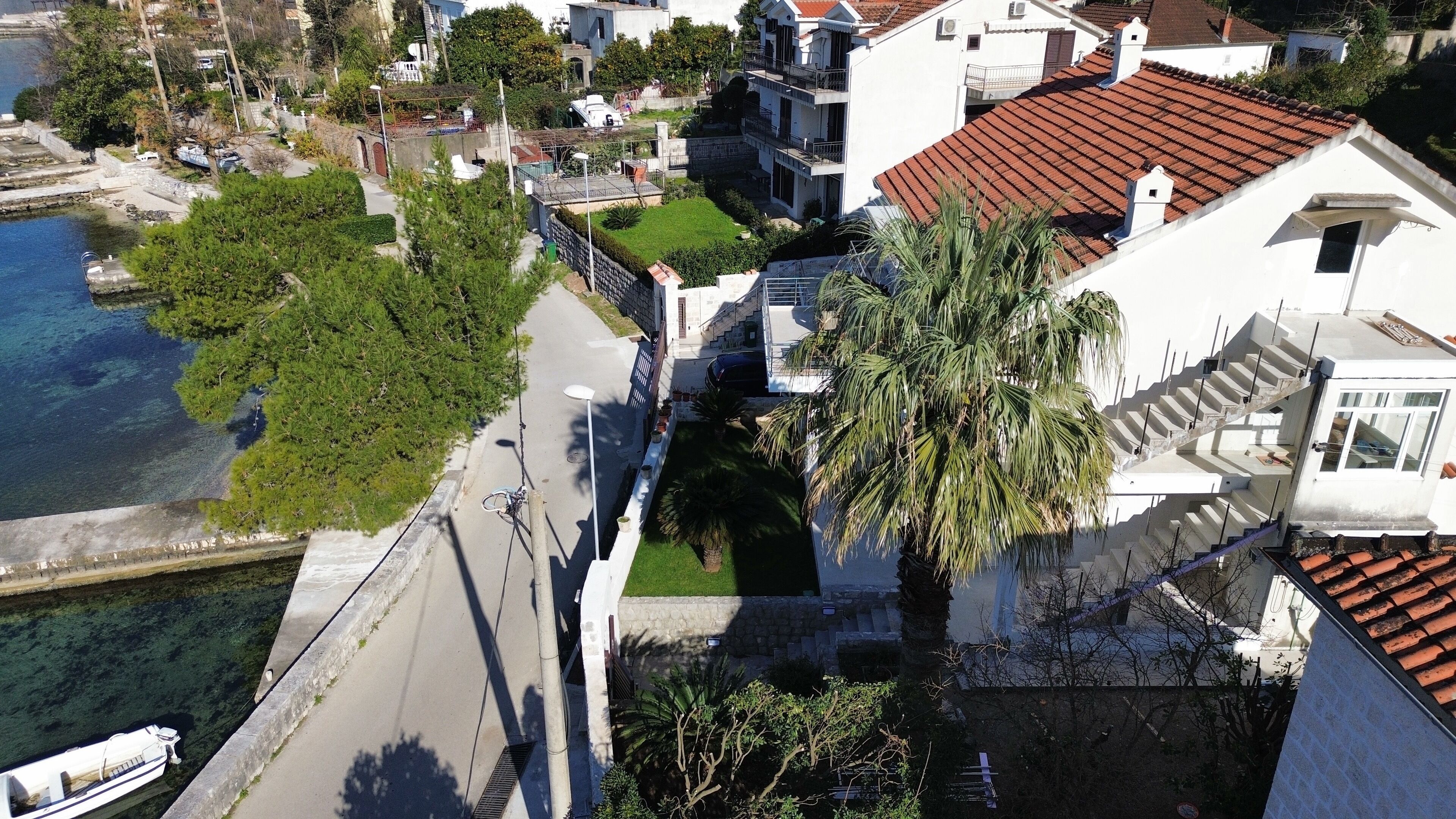 Vista aérea de una zona residencial costera con una carretera despejada, una palmera y una masa de agua.