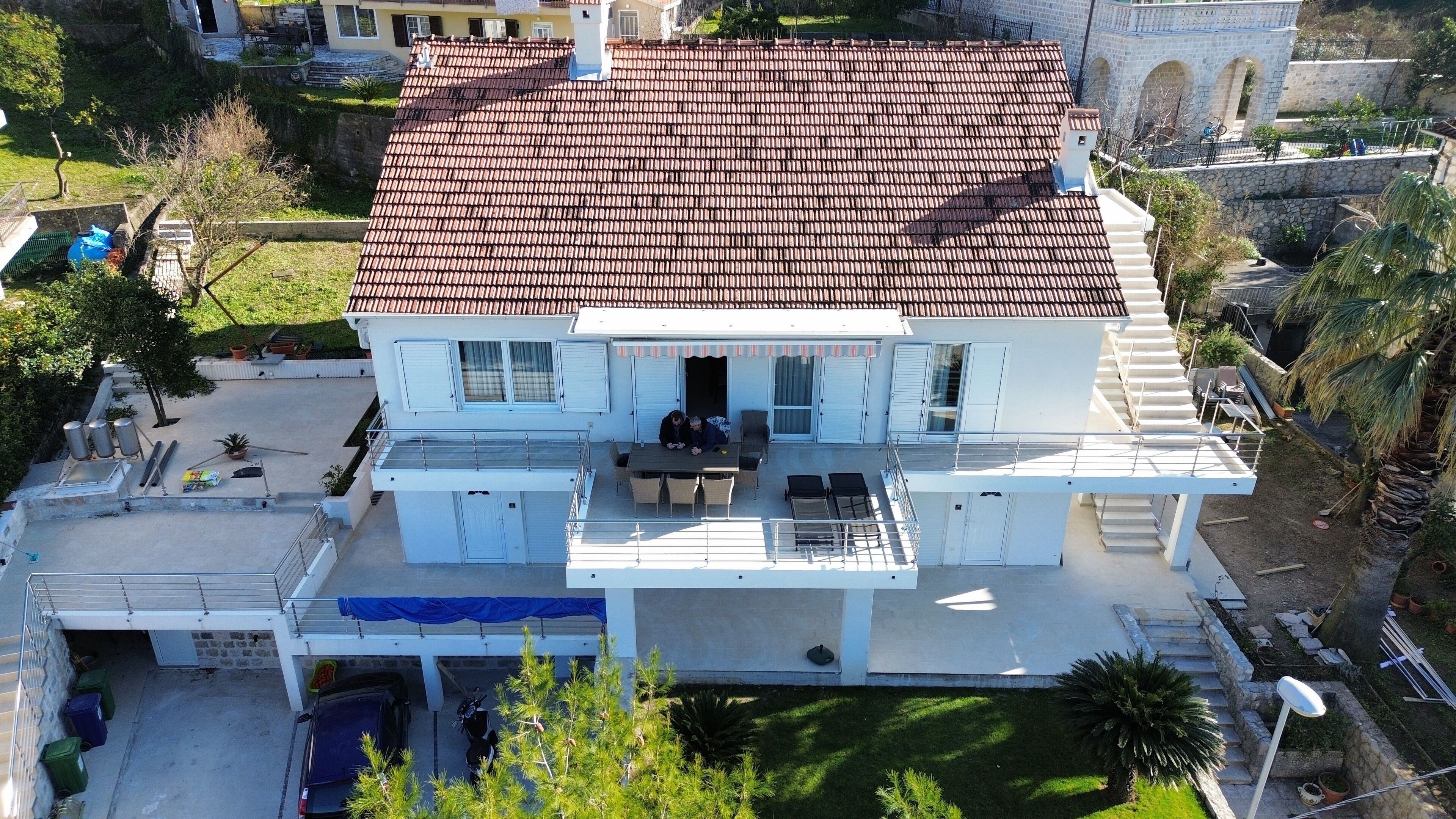 A two-story house with a tiled roof, a balcony, and a covered patio area.