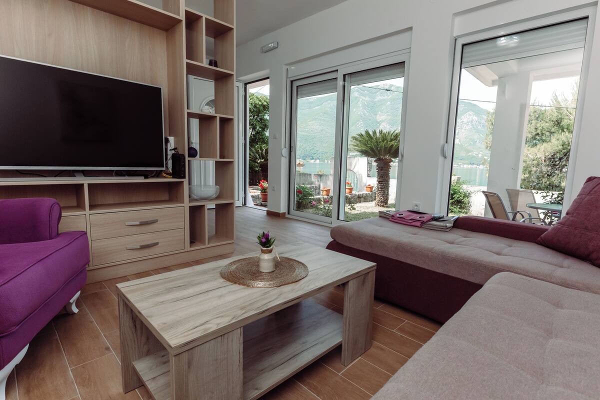 Uma sala de estar moderna com televisão de tela plana, prateleiras de madeira, um sofá e uma mesa de centro.