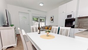 Eine moderne Küche mit weißen Schränken, einem Esstisch mit Stühlen und einer Couch im Hintergrund.