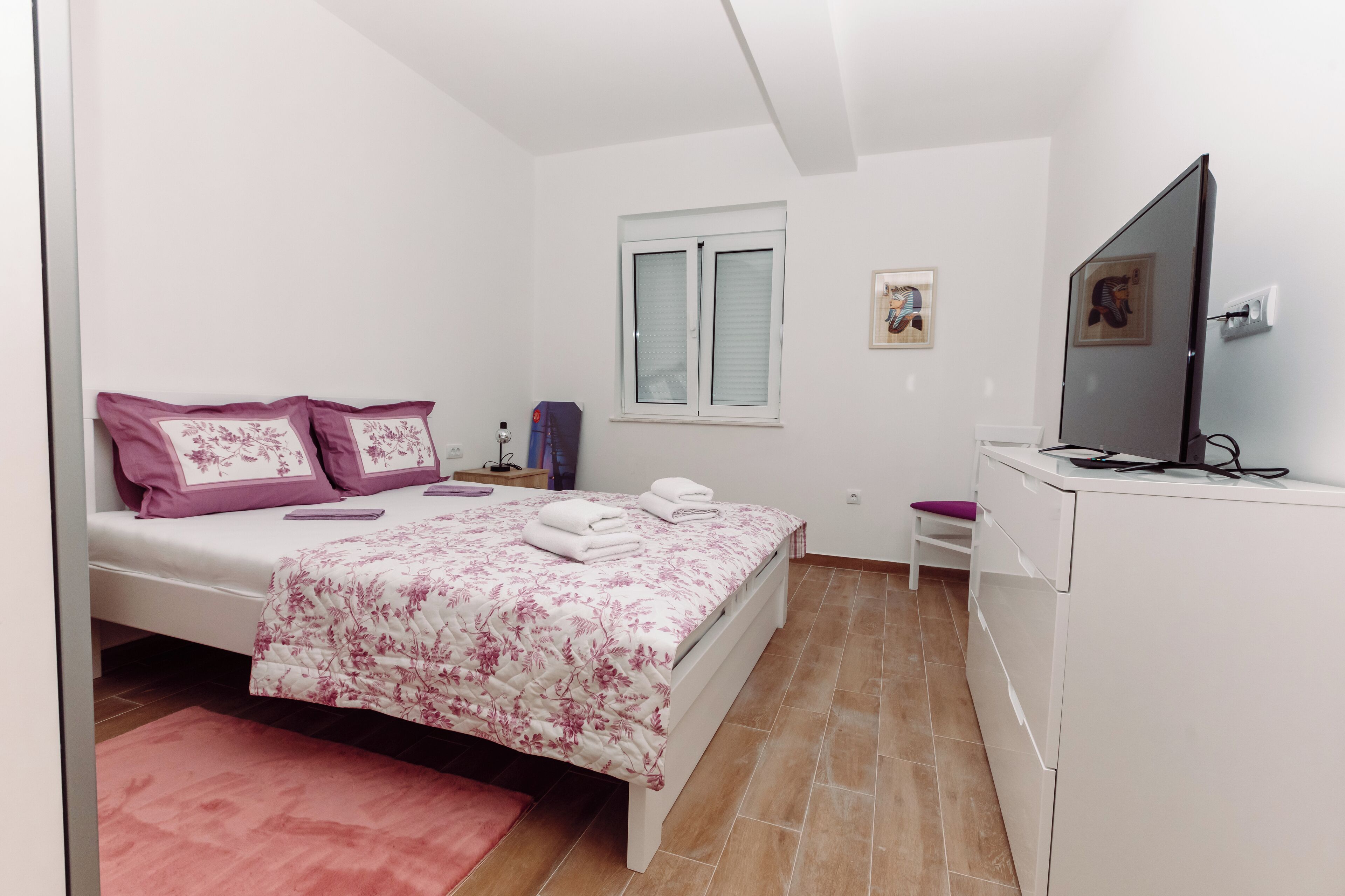 Un dormitorio con cama, escritorio, silla, televisor y ventana.