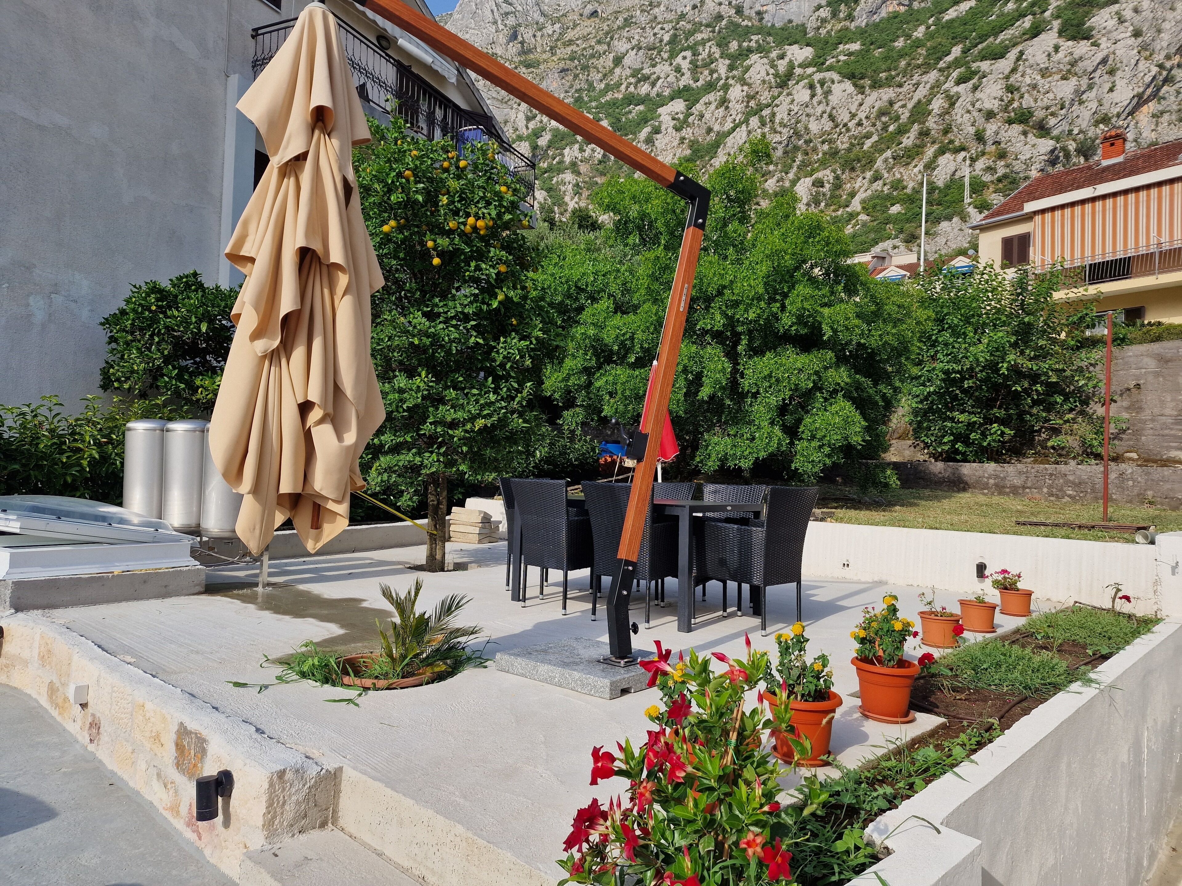 Eine Terrasse im Freien mit Tisch und Stühlen, umgeben von Blumentöpfen und einer Holz-Pergola.