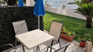 Eine Terrasse mit Tisch und Stühlen, einem blauen Sonnenschirm und Blick auf einen See mit einem Boot.