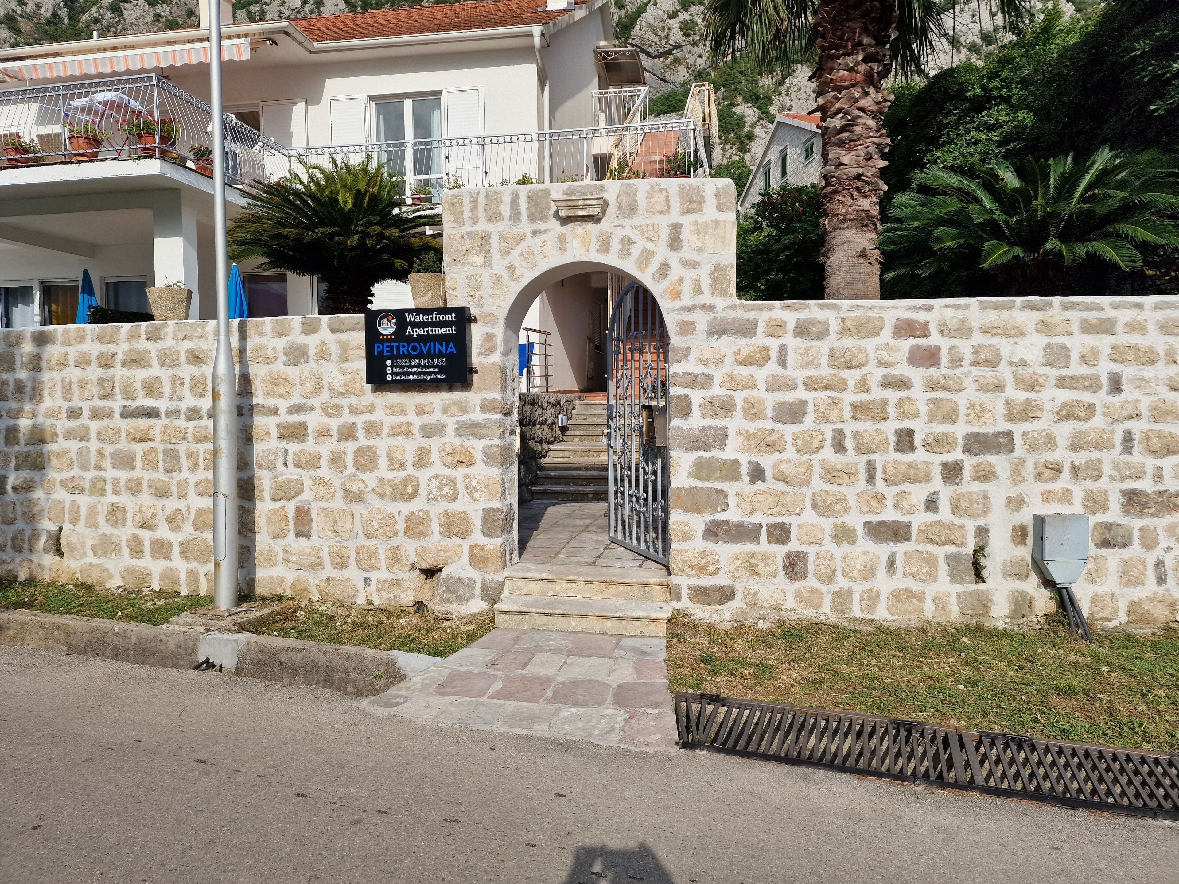 Una entrada de muro de piedra a un edificio, con un letrero que indica que se trata de un apartamento frente al agua llamado PETROVINA.