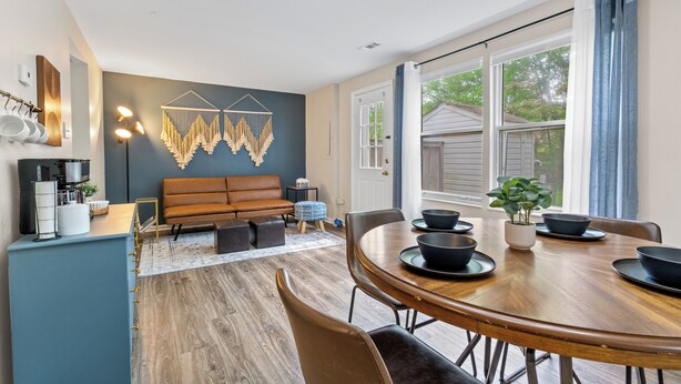 Un espace repas moderne avec une table et des chaises en bois, une décoration murale et une grande fenêtre agrémentée de rideaux.