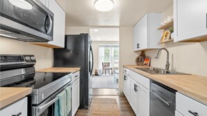 Une cuisine moderne équipée d’un four à micro-ondes, d’une cuisinière et d’un lave-vaisselle encastrés. On y trouve un plan de travail en bois, un évier et un tapis qui mène à un coin repas.