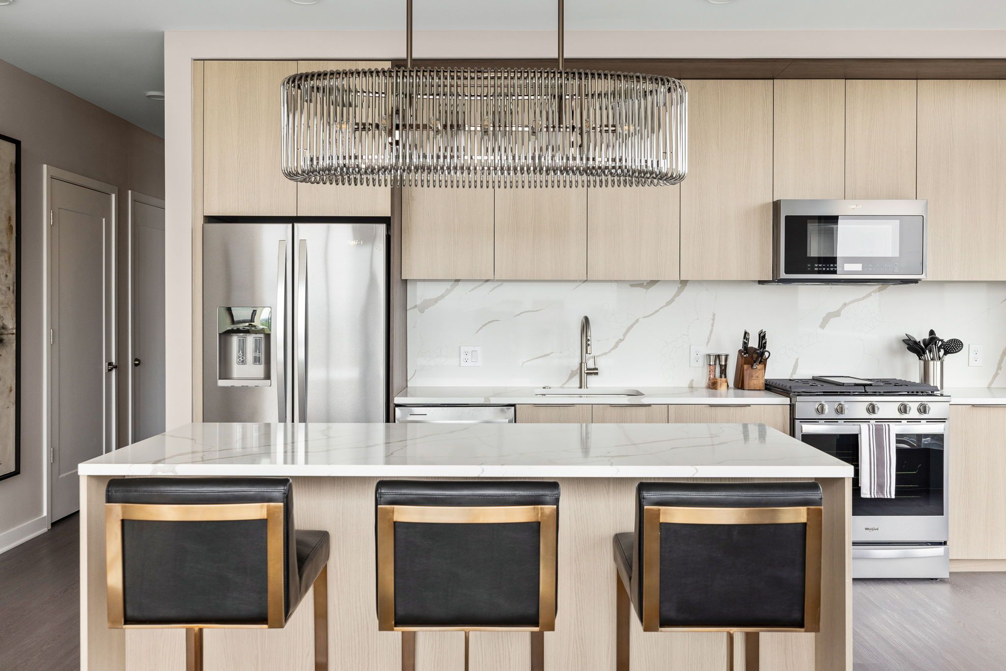 Une cuisine moderne dotée d’un îlot central, d’appareils électroménagers en acier inoxydable et d’un luminaire suspendu.