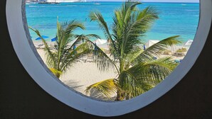 Vista circolare di una spiaggia con acque cristalline turchesi, palme e una nave da crociera in lontananza.
