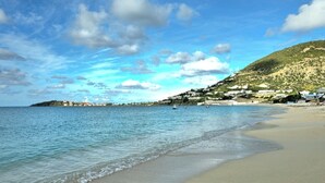 Una spiaggia con acque cristalline, una costa sabbiosa e un pendio con edifici.