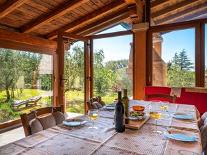 Enjoy meals in this dining area with a table set for two, featuring a tablecloth, plates, glasses, and a bottle of wine, with a view of the lush garden and trees.