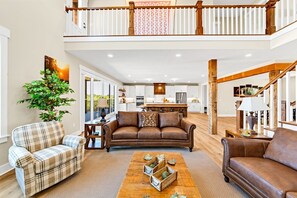 A spacious living area with a high ceiling, a wooden staircase, and a kitchen in the background. - Heavenly View | Hocking Hills, Pool, Theater (Logan)
