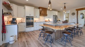 A modern kitchen with white cabinetry, stainless steel appliances, and a central island with stools. - Heavenly View | Hocking Hills, Pool, Theater (Logan)