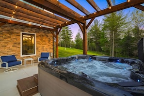 A hot tub under a wooden pergola with stone walls and a view of a golf course.