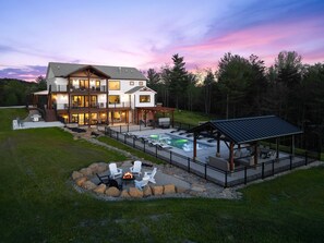 Une maison à plusieurs étages dotée d’une grande terrasse extérieure, d’une piscine et d’un espace aménagé avec un foyer.