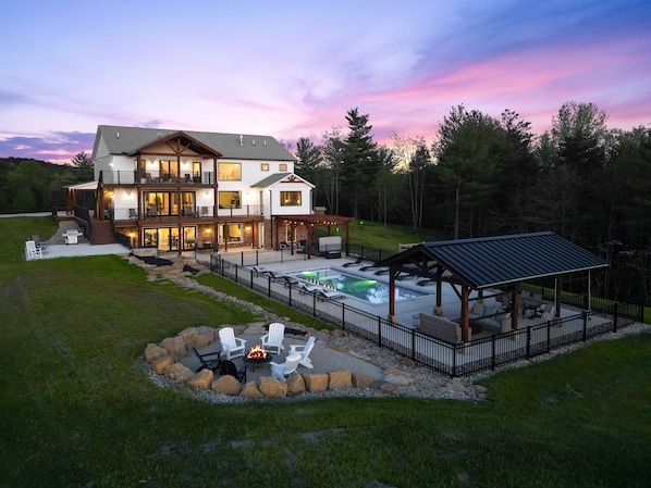 A multi-story house with a large outdoor deck, a swimming pool, and a fire pit area.