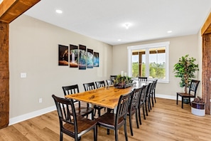 A dining area with a wooden table and chairs, a large window with a view, and a wall-mounted art piece. - Heavenly View | Hocking Hills, Pool, Theater (Logan)